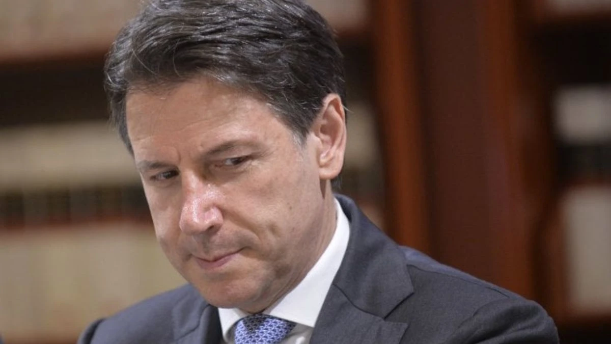 Giuseppe Conte in primo piano, volto teso, sfondo rosso acceso. Notte difficile per il Movimento 5 Stelle